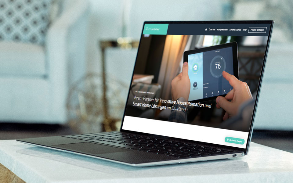 Webdesign Saarland - InnoHomes. Aufgeklappter Laptop steht auf einem Tisch in modernem Wohnzimmer und zeigt die Startseite einer Website für Smart Home Lösungen.